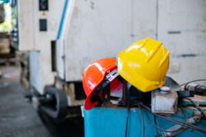 Cascos de seguridad naranja y amarillo apoyados sobre maquinaria industrial en entorno de trabajo.