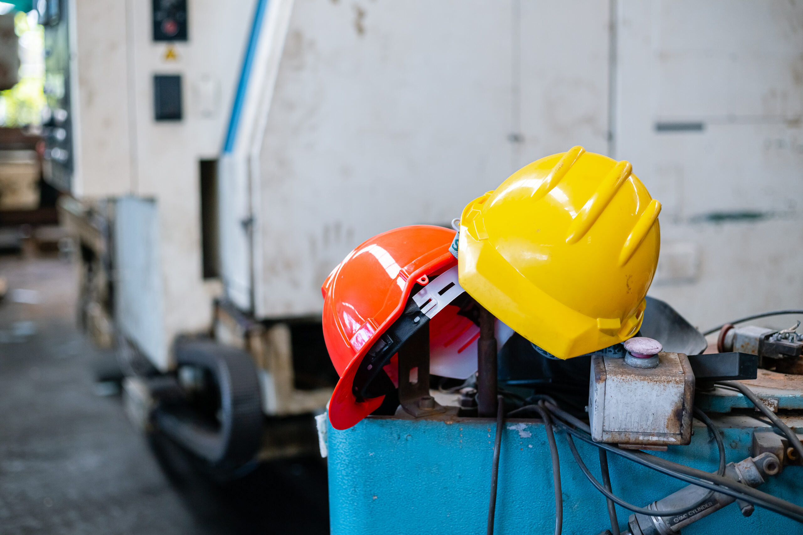 Cascos de seguridad naranja y amarillo apoyados sobre maquinaria industrial en entorno de trabajo.