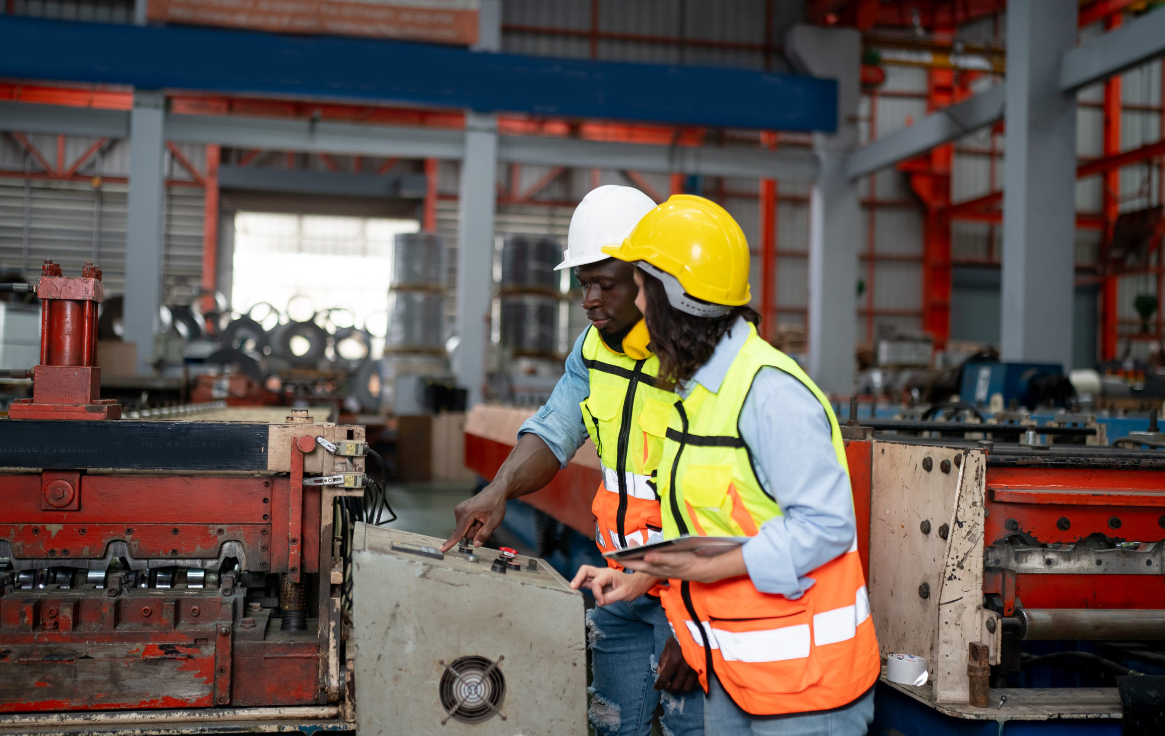 Dos técnicos con cascos y chalecos reflectantes revisando normativa de seguridad en nave industrial. 